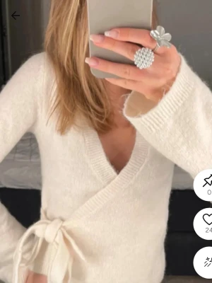 Vit omlottstickad tröja - Mysig vit omlottstickad tröja med knytband i midjan och djup v-ringning. Tröjan har långa ärmar och är gjord i ett fluffigt, mjukt material som ger en avslappnad men ändå trendig look.