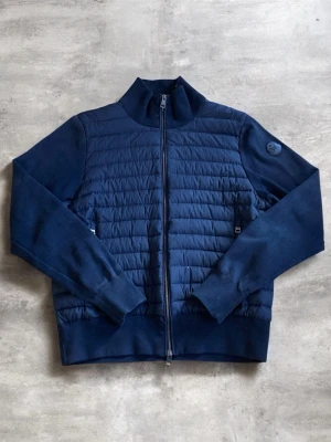 Svart cardiganjacka från Moncler - Snygg svart cardiganjacka från Moncler med quiltad front och mjuka ärmar. Jackan har hög krage, hel dragkedja och två sidofickor. Moncler-logga i svart på ärmen ger en exklusiv touch. Perfekt för lager på lager och stilrena outfits.