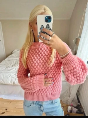 Populär rosa tröja - Säljer en rosa stickad tröja med bubbelmönster och ballongärmar. Tröjan har rund halsringning och ribbade muddar vid ärmslut och nederkant. Perfekt för dig som gillar trendiga och mysiga plagg.
