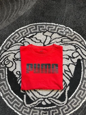 Röd PUMA t-shirt med logga - Snygg röd t-shirt från PUMA med stor svart logga framtill. Klassisk rund halsringning och korta ärmar. Tillverkad i mjuk bomull som känns skön mot huden. Perfekt för dig som gillar sportiga och stilrena plagg.