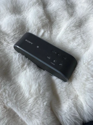 Sony trådlös högtalare svart NFC - Snygg och smidig trådlös högtalare från Sony i svart färg. Högtalaren har en avlång, rundad form och är tillverkad i plast och metall. Utrustad med NFC och Bluetooth för enkel parkoppling samt tydliga knappar för volym och uppspelning.