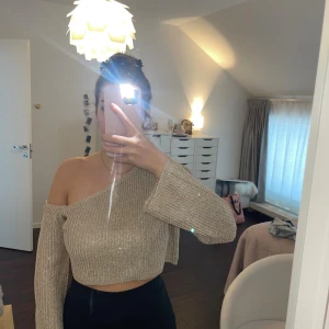 Glittrig beige offshoulder croppad topp - Säljer en glittrig guld offshoulder topp med lång ärm och croppad passform.  Köpt på vinted, vet ej märke eller storlek men sitter som en Xs/S 