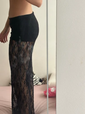 Svarta spetsleggings med låg midja - Säljer ett par svarta leggings i genomskinlig spets med låg midja. De har ett snyggt blommigt spetsmönster och är vida i benen för en trendig look. Perfekta för dig som vill sticka ut och gillar statement-plagg.