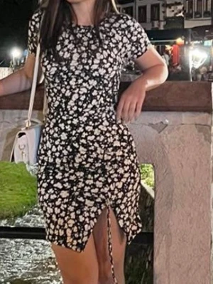 Svart blommig kortklänning - Svart kortklänning med vita blommor och snörningsdetalj framtill. Klänningen har rund halsringning och korta ärmar. 