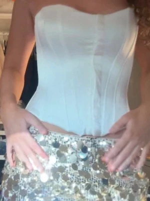 Zara korset - Snygg vit korsett i satin med formade kupor och markerade sömmar för en smickrande siluett. Axelbandslös modell som ger en elegant look och passar perfekt till olika outfits. Materialet har en lätt glansig finish som känns lyxig.