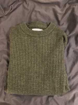 Olivgrön ribbstickad tröja från Volt - Säljer en olivgrön ribbstickad tröja med rund halsringning och långa ärmar. Tröjan har en klassisk, enkel design och är perfekt för lager på lager. Materialet ser mjukt och bekvämt ut, och färgen är lätt att matcha med andra plagg.