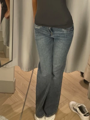 Blå bootcut jeans med låg midja - Säljer ett par klassiska blå bootcut jeans med låg midja och femficksmodell. Jeansen har en snygg tvätt och raka ben som blir vidare nedtill. Perfekta för sopiga outfits och funkar till sneakers eller boots.