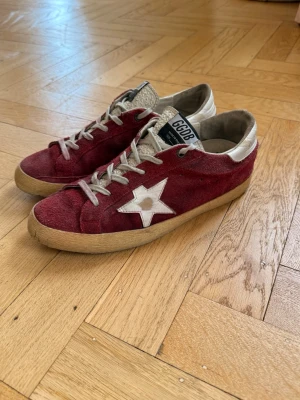 Röda golden goose skor - Snygga röda sneakers från Golden Goose med ikonisk vit stjärna på sidan. Ovandelen är i mocka och insidan är fodrad i textil. Perfekta för dig som gillar streetstyle och unika detaljer. Skorna är relativt slitna specifikt vid hälarna, därav priset. Nypris 5600kr. Inget OG medföljer. Pris kan diskuteras. Hör av er vid frågor och funderingar. 