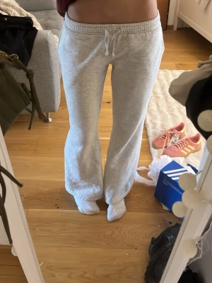 Ljusgråa mjukisbyxor med broderad ficka - Säljer ett par ljusgrå mjukisbyxor med dragsko i midjan och raka ben. Byxorna har en broderad detalj på bakfickan och är gjorda i mjukt, bekvämt sweatshirttyg. Perfekta för chill dagar eller när du vill vara extra comfy. För mig som är 167 så är de lite lite korta 