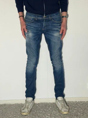 Blå slim fit dondup jeans med schyssta slitningar - Snygga blå slim fit jeans med lätt slitna detaljer och tvättad look. Jeansen har klassisk femficksdesign och normal midja. Perfekta för en avslappnad och trendig stil.