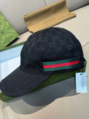 Gucci keps - Snygg svart keps från Gucci med klassiskt GG-monogram över hela kepsen och en grön-röd rand på sidan. Kepsen har böjd skärm och justerbar rem bak. Tillverkad i slitstarkt tyg som känns lyxigt och trendigt.