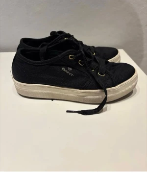 Svarta låga sneakers från Gant - Söjer dessa skor för dem har blivt för små!!💞Snygga svarta sneakers från Gant med vita sulor och guldfärgade öljetter. Skorna har klassisk låg modell och är tillverkade i textil med snörning framtill. Perfekta för en avslappnad och stilren look.