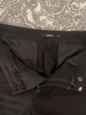 Svarta kostymbyxor från BikBok - Snygga svarta kostymbyxor från BikBok i bootcut. Byxorna har diskreta fickor bak, och stängs med dragkedja och knapp. Perfekta för en clean och stilren look. Materialet känns mjukt och följsamt. Modellen Vilma så midwaist. Säljer för att dom är förstora