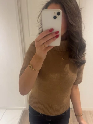 Beige stickad tröja med kort ärm - Snygg beige stickad tröja med korta ärmar och hög krage. Tröjan har ribbstickade muddar vid ärmslut och nederkant. Perfekt för lager-på-lager och passar till både jeans och kjol.