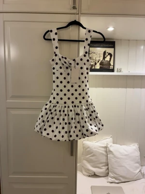 Vit prickig klänning från Zara - Supersöt vit klänning från Zara med svarta prickar och breda axelband. Klänningen har en kort, voluminös kjol och en lätt rynkad detalj vid bysten. Perfekt för dig som gillar lekfulla och trendiga plagg.