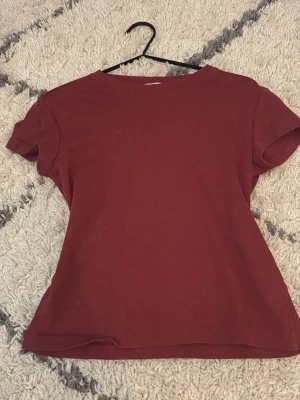 Mörkröd t-shirt från Bershka - En enkel och stilren mörkröd t-shirt från Bershka. T-shirten har rund halsringning och korta ärmar. Tillverkad i mjuk bomull som känns skön mot huden. Perfekt att matcha med jeans eller kjol för en avslappnad look.