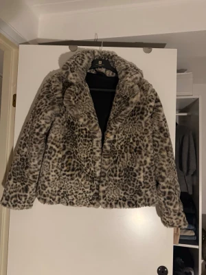 Leopardmönstrad pälsjacka - Snygg leopardmönstrad pälsjacka i fuskpäls med bred krage och långa ärmar. Jackan har en cool och trendig look, perfekt för dig som vill sticka ut. Färgerna går i beige, brunt och svart. Stängs framtill och har en mjuk insida.