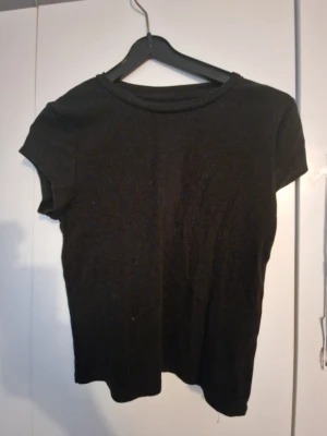 Svart croppad t-shirt - En enkel svart croppad t-shirt med rund hals och korta ärmar. Perfekt basplagg som passar till allt och är lätt att styla. Tillverkad i mjukt material för en bekväm känsla.