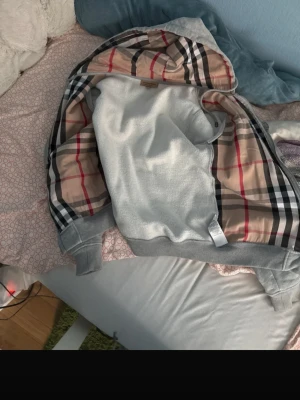 TRADEAR MIN Gråa Burberry zipper - Vill gärna byta ut denna mot någon ss Valentino, Moncler, Ysl osv... Snygg grå hoodie från Burberry med klassiskt rutigt foder i huvan och dragkedja framtill. Broderad logga på ärmen och ribbade muddar. Tillverkad i mjukt bomullsmaterial för skön känsla. Perfekt för dig som vill ha en stilren och exklusiv look.