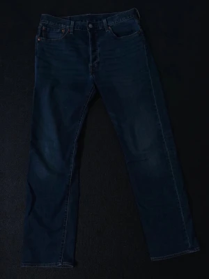 Levi's 501 mörkblå jeans - Klassiska Levi's 501 jeans i mörkblå denim med raka ben och fem fickor. Snygg vintagekänsla och ikonisk läderpatch bak i midjan. Perfekta för dig som gillar tidlös stil och vill ha ett par derived jeans som funkar till allt.