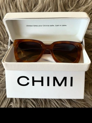 Bruna solglasögon från CHIMI - Snygga solglasögon från CHIMI i en brun, transparent ton. Modellen har en fyrkantig form och breda bågar som ger en modern look. Kommer i originalförpackning med vit hård ask. Perfekta för dig som vill ha en stilren accessoar.