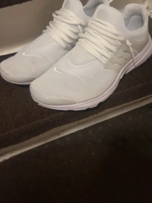 Nike vita Presto sneakers - Nike Presto sneakers i helvitt med mesh- och syntetmaterial, klassisk låg modell med rund tå och vita skosnören. Snygg minimalistisk design med diskret Nike-logga på sidan och tåpartiet. Perfekta för dig som gillar stilrena och sportiga sneakers.