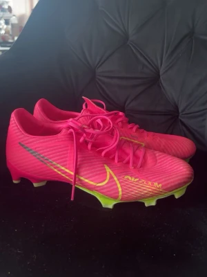 Nike Mercurial rosa fotbollsskor - Säljer ett par Nike Mercurial fotbollsskor i en riktigt snygg rosa färg med gula detaljer och silverfärgad swoosh. Skorna har snörning och dobbar för spel på gräs. Tillverkade i syntetmaterial för lätt vikt och bra bollkontroll. Perfekta för dig som vill sticka ut på planen.