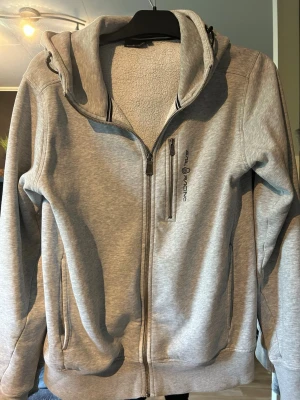 Grå hoodie från Sail Racing - Snygg grå hoodie från Sail racing. Perfekt för en chill dag o slapp. På ena armen vid handleden så är den sydd eftersom stygnen åkte upp men man märker inte av det. Det finns också en lite prick på ryggen som är okänd men går säkert att fixa med stålull.
