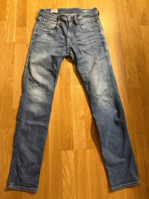 Blå jeans från Replay med raka ben - Säljer ett par klassiska blå jeans från Replay med raka ben och snygga slitningar framtill. Jeansen har fem fickor, dragkedja och knappgylf samt Replay-logga på myntfickan. Tillverkade i bomull med en skön passform.