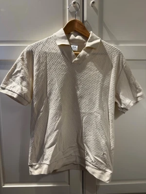 Beige kortärmad polotopp från Zara - Snygg beige polotopp från Zara med korta ärmar och subtilt strukturmönster i tyget. Toppen har en klassisk krage och v-ringning, perfekt för en stilren look. Tillverkad i mjukt material som känns skönt mot huden.
