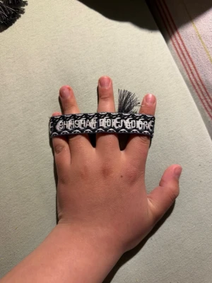 Svart-vitt armband  - Snyggt svart och vitt armband  med broderad logga och dekorativa fransar. Armbandet har en bred, vävd design som ger en cool och trendig look. Perfekt accessoar för att lyfta din outfit.