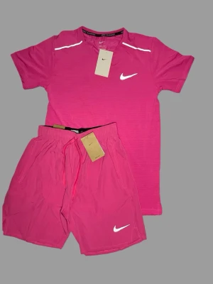 Rosa träningsset från Nike - Säljer ett sportigt rosa träningsset från Nike med t-shirt och shorts. Setet har reflekterande detaljer på axlarna och logga på shortsen. 