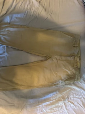 Beige chinos från Levi's - Snygga beige chinos från Levi's med klassisk rak passform. Byxorna har två sidofickor fram och två bakfickor med knapp, samt bälteshällor. Perfekta för en stilren och avslappnad look. Materialet är mjukt och bekvämt, passar till många olika outfits.