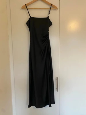 Svart silkes långklänning  - Elegant svart långklänning med smala axelband och draperad detalj i sidan. Klänningen är tillverkad i ett glansigt, mjukt material som ger en lyxig känsla. Från Zara i strl XS🌸