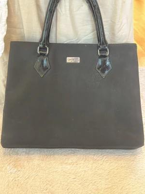 Svart väska från DKNY - Svart handväska från DKNY i bra skick. Väskan har mycket utrymme med tre stora fack.Perfekt för dig som gillar klassisk och enkel design.