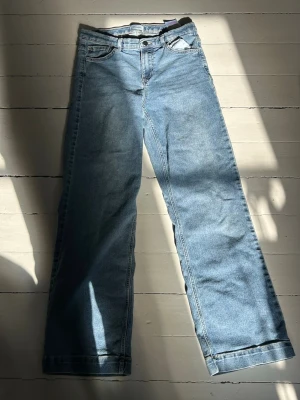 Ljusblå raka jeans - Säljer ett par ljusblå jeans med rak passform och klassisk femficksdesign. Jeansen har normal midja och är tillverkade i denim. Perfekta för en avslappnad och trendig look.