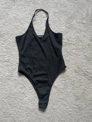Svart halterneck body  - Snygg svart body med halterneck och djup urringning. Klassisk modell med hög benskärning och smala axelband som knyts i nacken. Perfekt för stranden eller poolen. Materialet är stretchigt och följsamt.