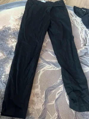 Svarta kostymbyxor från La Redoute - Snygga svarta kostymbyxor från La Redoute edition. Byxorna har rak passform och klassisk midja, perfekta till en stilren look. Tunt och mjukt tyg som ger en dressad känsla. Passar dig som gillar enkel och tidlös stil. Korta i benen så OBSERVERA!