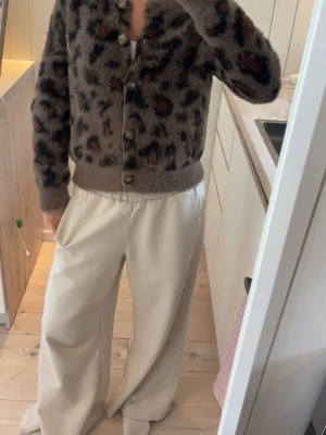 Brun leopardmönstrad kofta - Mysig brun kofta med leopardmönster och stora knappar framtill. Koftan är fluffig och har ribbade muddar vid ärmslut och midja. Perfekt för dig som gillar djurmönster och vill ha en trendig look.