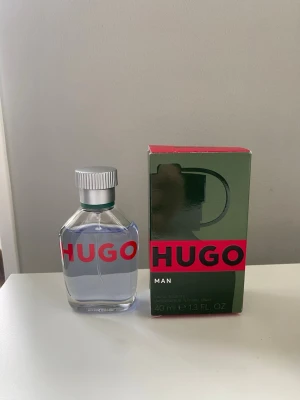 Hugo Boss Man Eau de Toilette 40ml - Fräsch parfym från Hugo Boss, Hugo Man, i en stilren transparent glasflaska med silverfärgad kork och röd logga. Kommer i originalkartong i grönt och rött. Flaskan rymmer 40 ml och är perfekt för dig som gillar klassiska dofter.