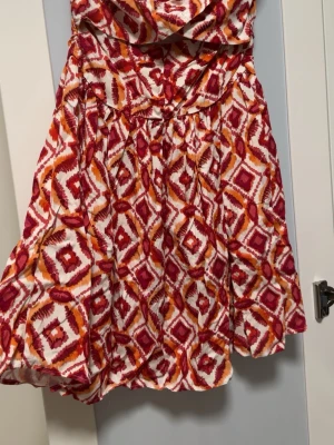 Mönstrad kort klänning i rött och orange - Kort klänning utan armar med ett fint mönster. Helt ny, oanvänd 🧡 Skickar gärna fler bilder om det behövs :)