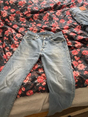 Levi's 501 ljusblå jeans W32 L32 straight leg - Klassiska Levi's 501 jeans i ljusblå denim med raka ben och knappgylf. Jeansen har fem fickor och den ikoniska läderpatchen bak i midjan. Perfekta för en avslappnad och tidlös stil. Säljes pga för liten storlek