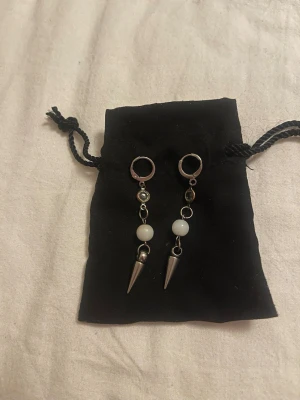 Silvriga örhängen med pärlor och spikes - Coola örhängen med silvriga ringar, vita pärlor och metallfärgade spikes. Hängande design som ger en edgy vibe. Perfekta för att lyfta din stil med en unik touch. Obs! Har rostat lite upptill men inget som syns så mycket. 