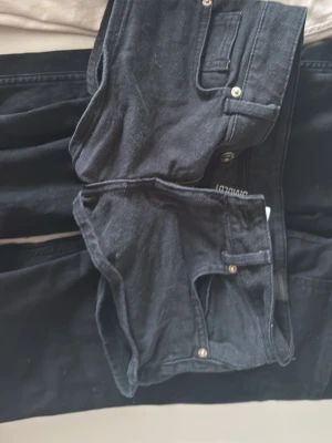 Svarta lågmidjade shorts  - Säljer ett par svarta jeans från Divided med klassisk femficksmodell och raka ben. Jeansen har knappgylf och är tillverkade i ett mjukt bomullsmaterial med lite stretch. Perfekta för en avslappnad och stilren look.