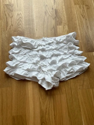 Vita mini shorts med volang - Säljer ett par vita mini shorts med flera lager volanger och elastisk midja. Perfekta för dig som vill ha en lekfull och trendig look. Mjukt stretchigt material💞💞