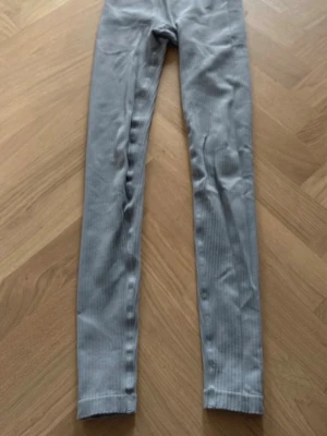 Grå ribbade leggings med hög midja - Snygga grå leggings med ribbad struktur och hög midja. De är stretchiga och sitter tajt längs benen, perfekta för en trendig och bekväm look. Materialet är mjukt och följsamt, vilket gör dem sköna att bära hela dagen.