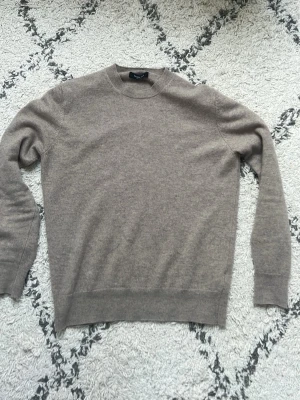 Beige Kashmir tröja från Massimo Dutti - Stilren beige Kashmir tröja från Massimo Dutti i mjukt material. Tröjan har rund halsringning, långa ärmar och ribbade muddar vid ärmslut och nederkant. Perfekt för en clean och klassisk look.
