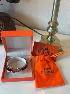 Hermès armband  - Snyggt armband från Hermès i svart emalj med silverfärgad H-detalj framtill. Kommer i original ask och orange tygpåse med logga. Perfekt accessoar för att lyfta din outfit med en lyxig touch från Paris.