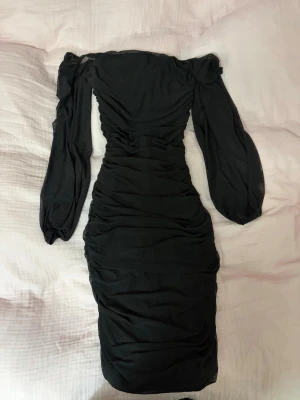 Svart offshoulder klänning med meshärmar - Svart medel lång klänning med långa transparenta meshärmar. Klänningen är rynkad längs hela baksidan och har en kedja i ryggen. Passar strl S och M