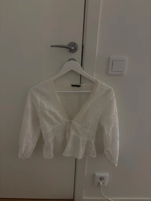 Vit spetsblus med volang - Söt vit blus med v-ringning och volang nertill. Blusen har trekvartsärmar och är dekorerad med broderad spets. Perfekt för en fräsch och romantisk look. Tvättas såklart innan skickning! Använd 1 gång.